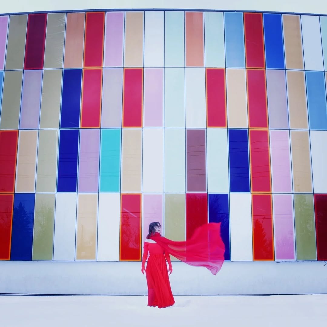 Sasha Kristoff in a red dress in front of a wall of coloured glass panels