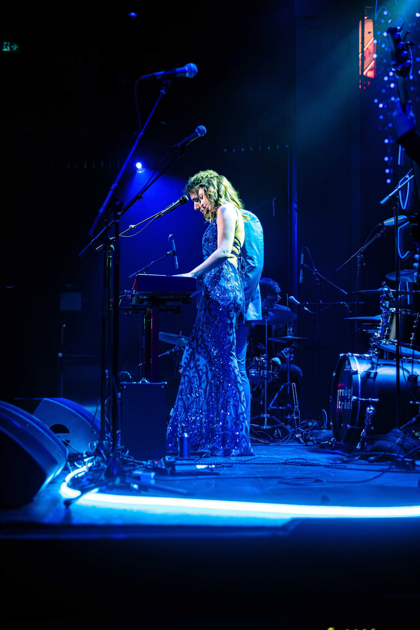 Sasha Kristoff at the keys in a sequined blue gown under blue stage light, the full stage at El Mocambo