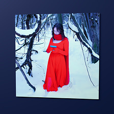 The Note Poster, an 18 by 18 inch matte print hung on a wall: Sasha in the red dress, holding the note she found in the snow