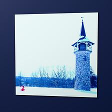 The Tower Poster, an 18 by 18 inch matte print hung on a wall: Sasha in red, small against the snow and the stone tower